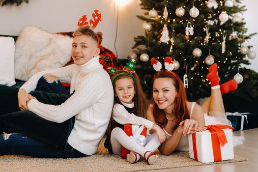 a happy family is lying on the floor of the house with New Year's gifts, next to the Christmas tree,