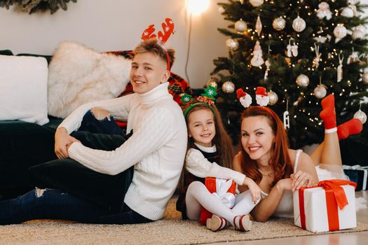 a happy family is lying on the floor of the house with New Year's gifts, next to the Christmas tree,