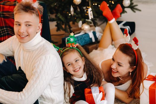 a happy family is lying on the floor of the house with New Year's gifts, next to the Christmas tree,