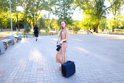 Young female tourist wearing dress standing outside with camera valise. Concept of photographer profession and summer season, tourism.