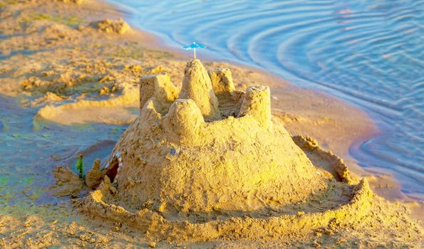 Beautiful sand castle illuminated by the morning sun on the beach of the tropical sea. The concept of a family vacation at sea.