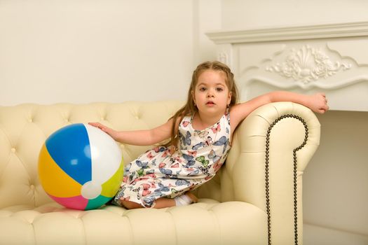 Adorable little girl playing with a ball on the sofa. Concept for family, advertising, happy childhood.