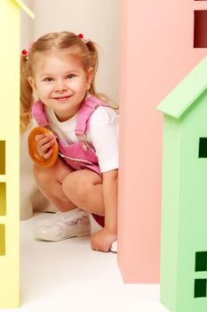 A cute little girl looks out from behind a toy wooden house. The concept of advertising children's products.
