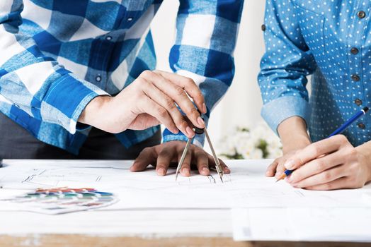 Professional designers discussing architecture project. Creative teamwork and project brainstorming. Close up human hands and construction drawing of building on desk. Industrial engineering company.