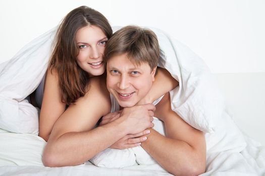 Beautiful young couple relaxing in bed at home over white