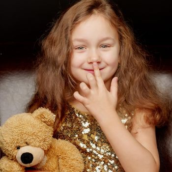 A nice little girl with a teddy bear. Studio photo on a black background. The concept of a happy childhood, publication on the cover of the magazine.