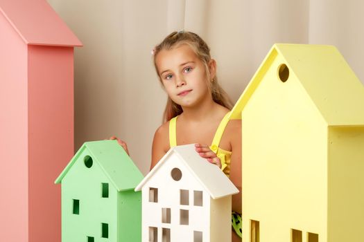 A cute little girl looks out from behind a toy wooden house. The concept of advertising children's products.