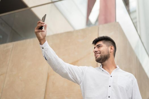 Young handsome hispanic man taking selfie with smartphone outdoors. High quality photo