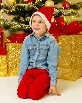 A cute little boy near a Christmas tree with a gift. Concept of family holidays, Happy childhood.