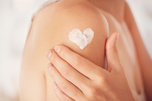 A young girl applies a moisturizer to her skin, a woman gently cares for her body, depicts a heart with a cream, taking care of herself, beauty and health.