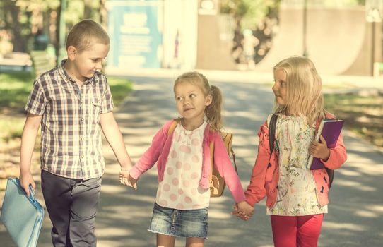Little pupils walking from school after lessons by holding hands