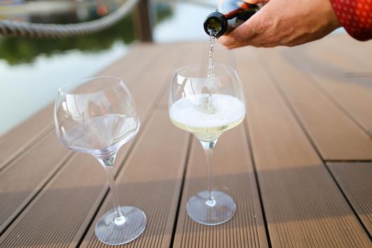 Male hands wearing red shirt pouring wine on wooden table. Concept of sommelier profession and alcohol.