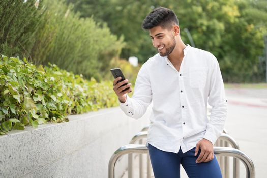 Handsome young man, smiling, using a mobile phone outdoors. High quality photo
