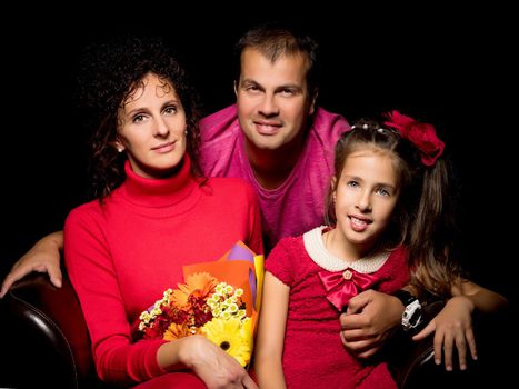 Family portrait, mom and dad with a charming little daughter. On a black background. The concept of family happiness.