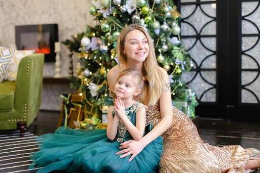 Young european woman and little daughter with bengal light sitting on floor near Christmas tree. Concept of celebrating New Year, winter holidays and fashion.
