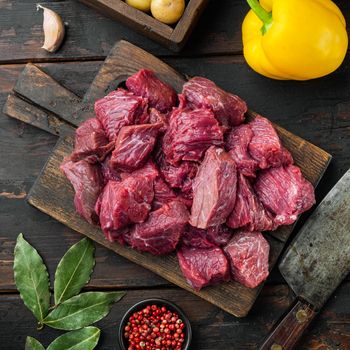 Raw meat diced for stew set with sweet bell pepper, on old dark wooden table, square format