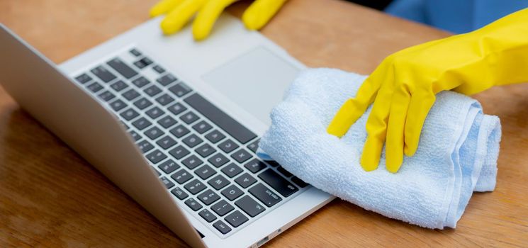 Hand of young asian woman cleaning and wipe laptop computer with disinfect and alcohol for protect pandemic covid-19 at home, girl in gloves cleaner notebook for hygiene, health care concept.