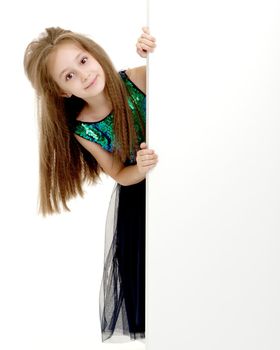 A nice little girl is looking because of an empty banner in which you can insert any text. The concept of a happy childhood, advertising, selling goods. Isolated on white background.