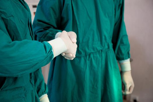 Teamwork of doctor and assistant handshake with success together at hospital, agreement and partner of surgeon, team of surgical shaking hands with confident at operation room, medical and health.
