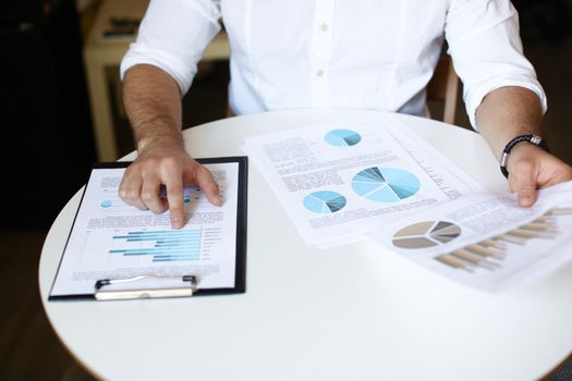 Male caucasian person working with documents and diagrams, wearing white shirt and watch.