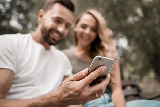 young couple watches a video on a smartphone sitting on a Park bench.people and technology