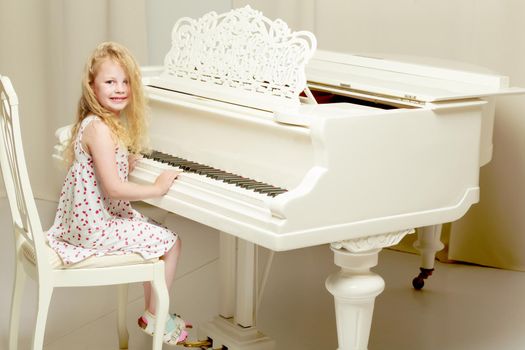 A nice little girl is playing on a big white piano. The concept of musical and aesthetic education of a child.