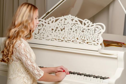 A teenage girl is playing on a white grand piano. The concept of creative development of personality, music education.