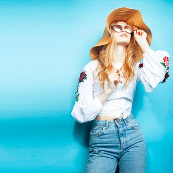 lifestyle people at summer vacation concept. young pretty smiling blond girl with long hair wearing lot of jewelry rings, sunglasses, hat posing cheerful on blue background close up