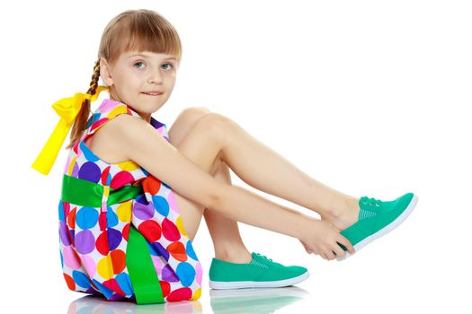 A beautiful Caucasian little blonde girl with long pigtails, in which large colored bows are braided, and a short bangs on her head. In a short summer dress, a pattern of multi-colored circles.