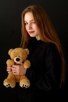 Beautiful teenage girl with a teddy bear on a black background. Concept layout for magazine cover.