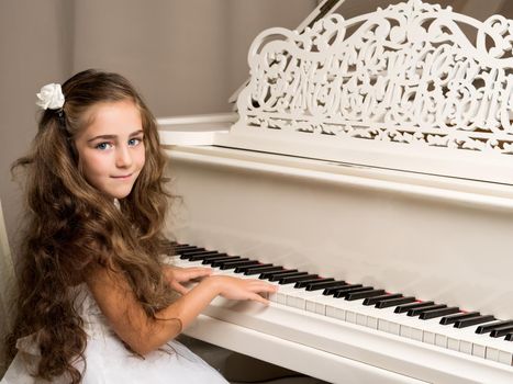 Beautiful little girl near a white grand piano. The concept of education and school, children's creativity.