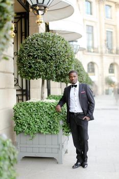 Afro americanmale person wearing suit and standing near tree in city. Concept of black businessman.