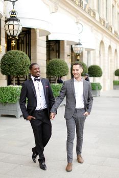 Afro american and caucasian stylish gays walking outside in city. Concept of same sex male couple.