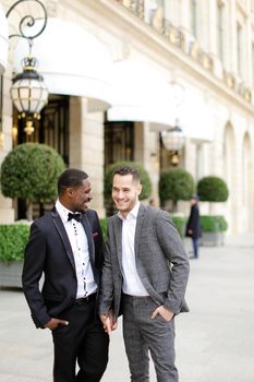 Afro american and caucasian smiling gays walking outside in city. Concept of same sex male couple.