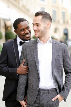 Afro american man hugging european boy wearing suit. Concept of gays and same sex couple.