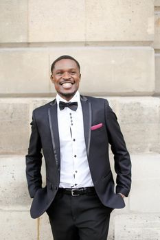 Afro american happy smiling man wearing dark suit and standing outside in wall background. Concept of black businessman.