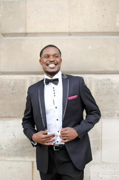 Afro american happy successful smiling man wearing dark suit and standing outside in wall background. Concept of black businessman.