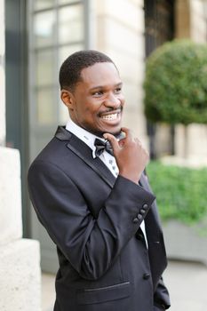 Afro american happy good looking male person wearing suit and smiling outside. Concept of black businessman.