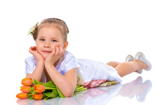 Charming little girl in a beautiful dress lies on the floor with a bouquet of tulips. Concept of happy people, childhood and holidays. Isolated on white background.