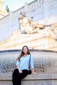 Young female tourist sitting near Trevi fountain, wearing blue shirt. Concept of traveling to Italy, Rome and youth.