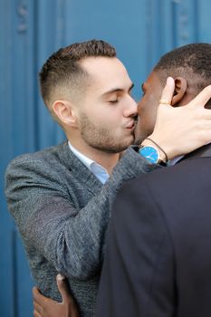 Caucasian handsome man kissing afro american guy in door background. Concept of lgbt, gays and same sex couple.