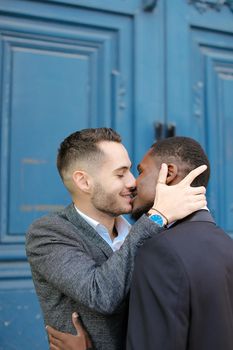 Caucasian man kissing afro american guy in door background. Concept of lgbt, gays and same sex couple.