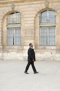 Afro american smiling man walking in city and wearing black suit. Concept of successful businessman and urban life.