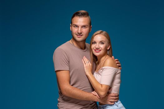 Young couple is hugging on blue background in studio. They wear T-shirts, jeans and smile. Friendship, love and relationships concept