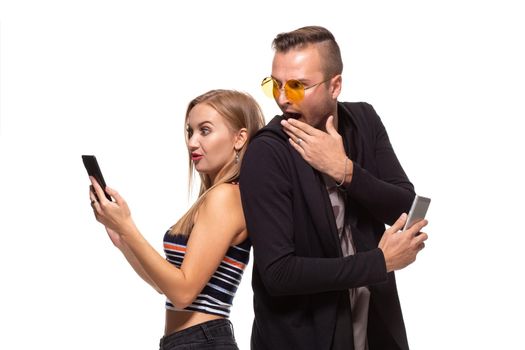 Man and woman stand with their backs to each other with telephones in their hands on white background. Studio shot