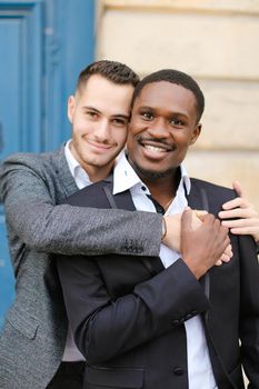 Portrait of two hugging boys, caucasian and afro american, wearing suits. Concept of gays and lgbt.