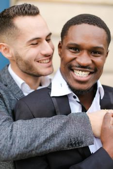 Portrait of two hugging smiling boys, caucasian and afro american, wearing suits. Concept of gays and lgbt.