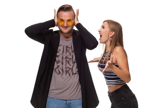Young family couple have conflict. Angry blonde young European woman gestures with hands, shouts at husband who is guilty, stands together against white background, have dispute and quarrel