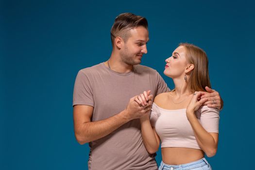 Young couple is hugging on blue background in studio. They wear T-shirts, jeans and smile. Friendship, love and relationships concept