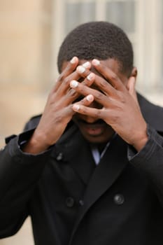 Portrait of afro american boy, closed eyes with hands. Concept of sad emotions and problems.